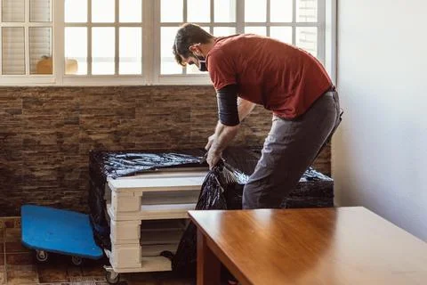 Worker removing plastic wrap from a piece of furniture in a moving operation Stock Photos