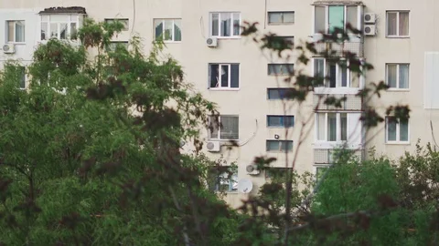 A worker is repairing a window in multi-storey residential building behind trees Stock Footage 107989796