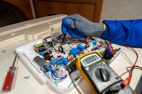 Worker repairs a circuit board with tools in a workshop during daytime hours Stock Photos