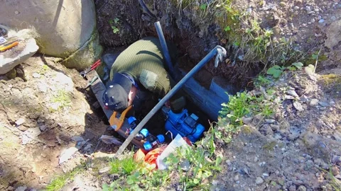 Worker repairs equipment in a hole at a construction site in daylight Stock Footage 337425789