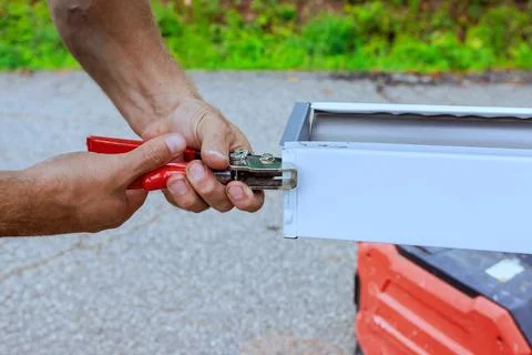 Worker repairs gutter metal structure using pliers while standing on gravel.. Stock Photos