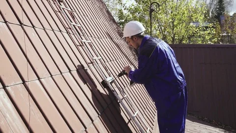 The worker repairs the ladder on the roof using a wireless drill 4k. Stock Footage 80241987