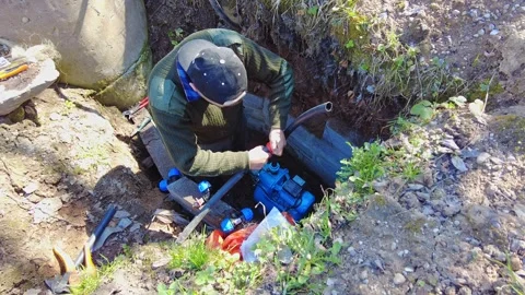 Worker repairs pump in trench during sunny day in rural area 스톡 동영상 337425862