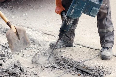 A worker repairs the road surface with a jackhammer on a summer day Stock Photos