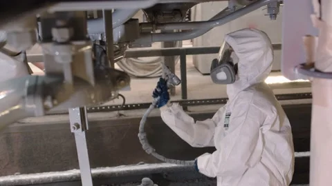 A worker in a respirator covers the metal structure of the machine with gray Stock Footage 196357777