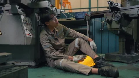 Worker rests after long shift, weary, head against machine Stockbeeldmateriaal 346268991