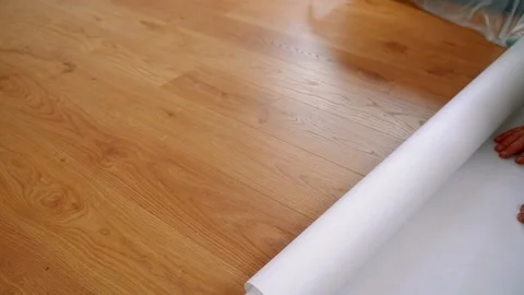 A worker rolls out a roll of white non-woven wallpaper on the wooden floor. Stock Footage 139742117