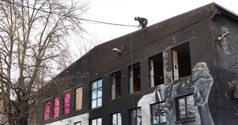 Worker on rooftop above graffiti-covered brick warehouse facade Stock Footage 321048942