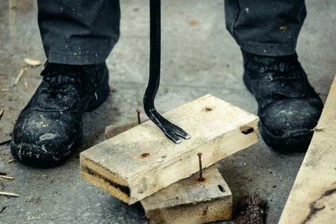 Worker in rough boots pulls nails out of wooden planks. Construction and repair. Foto stock