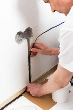 Worker runs new electrical wires into a cutout in a white apartment wall. T.. Stock Photos