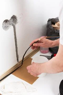 Worker runs new electrical wires into a cutout in a white apartment wall. Thi 写真素材