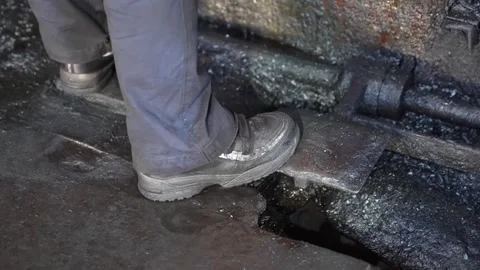 Worker safety boots stepping on wet industrial factory floor near heavy forging Stock Footage 336633217