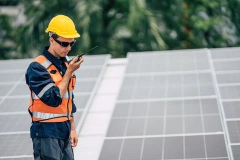 Worker in safety gear communicates while monitoring solar panels in a green.. Stock Photos