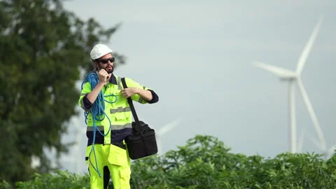 Worker in safety gear directs operations at wind farm construction site daylight Stock Footage 303616515