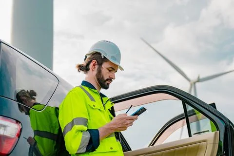 Worker in safety gear monitors data near wind turbines during daytime Stock Photos