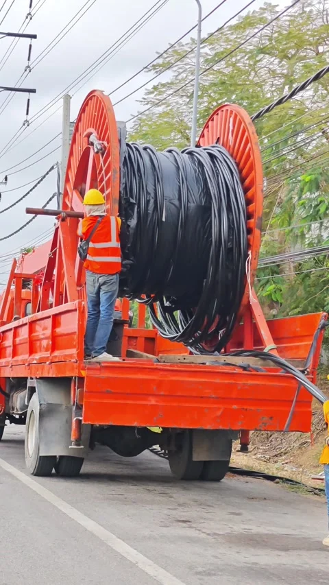 Worker in safety gear unrolling a massive spool of twisted aerial. Stock Footage 338175194