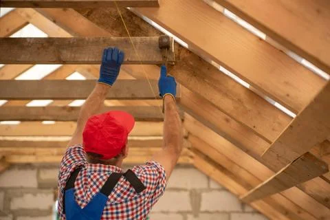 Worker in safety gloves constructing a new roof structure, hammering wooden.. Stock Photos