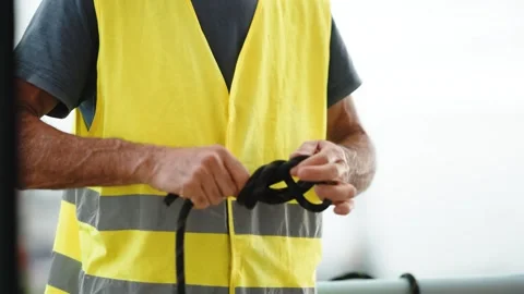 Worker in a safety vest coiling a black rope Stock Footage 346183406
