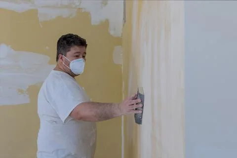 Worker sanding the drywall mud using sand trowel during renovation the house Photos