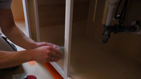 Worker sanding wooden cabinet surface by hand with sandpaper during renovation. Stock Footage 334019736
