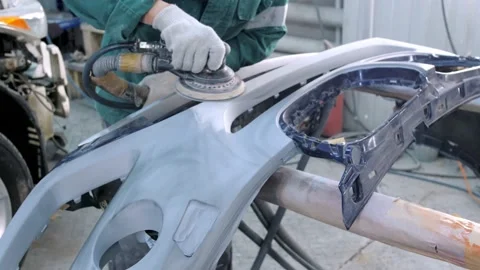 Worker sands bumper surface standing in car service garage Stock Footage 166576487