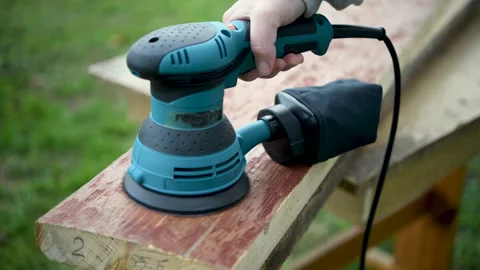 A worker sands old boards using an orbital sander. Stock Footage 321523421