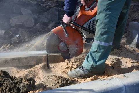 A worker saws a concrete block with a circular saw with a diamond blade. Stock Photos