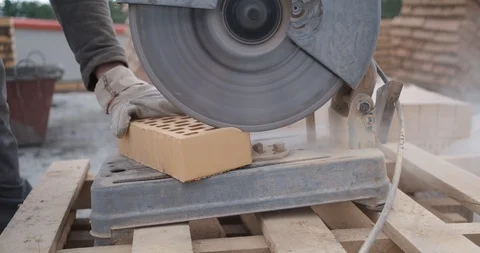 Worker saws facing brick with cutting disc, dust, corner is cut off from brick Stock Footage 117986175