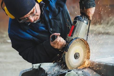 Worker saws metal with an old angle grinder. Selective focus. Outdoors Stock Photos