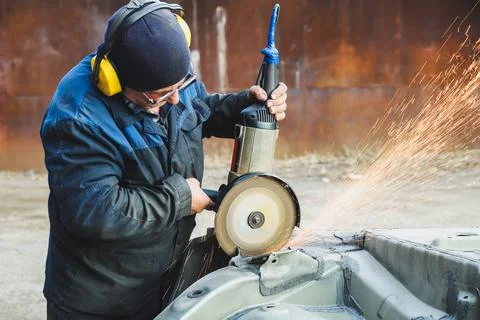 Worker saws metal with an old angle grinder. Selective focus. Outdoors Stock Photos