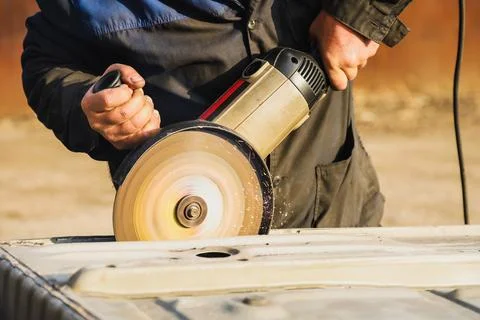 Worker saws metal with an old angle grinder. Selective focus. Outdoors Stock Photos