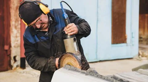 Worker saws metal with an old angle grinder. Selective focus. Outdoors Stock Photos