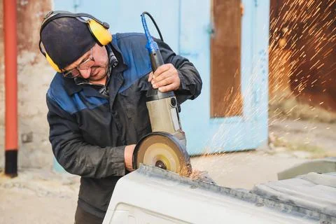 Worker saws metal with an old angle grinder. Selective focus. Outdoors Stock Photos
