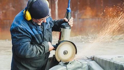 Worker saws metal with an old angle grinder. Selective focus. Outdoors Foto stock