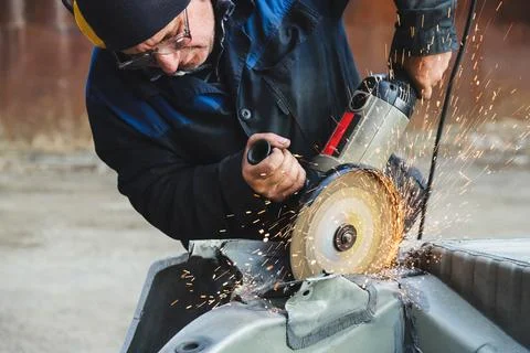 Worker saws metal with an old angle grinder. Selective focus. Outdoors Stock Photos