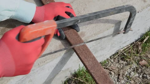 A worker saws off a square metal pipe with a hacksaw. Stock Footage 153307341