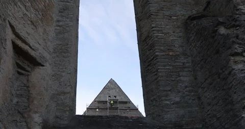 Worker on scaffolding restoring a Gothic ruin, framed by a dark stone arch. Stock Footage 320168894