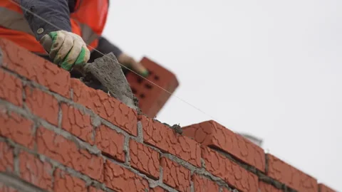 Worker scoops mortar onto brick line using small trowel Stock Footage 311891997