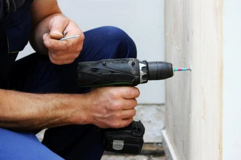 The worker screws screw with a screwdriver while decorating the window shutter. Stock Photos
