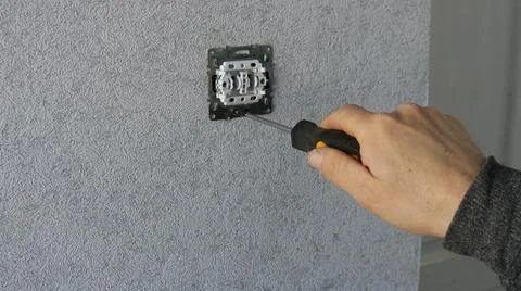 A worker screws a screw into a socket or light switch using a screwdriver Stock Photos