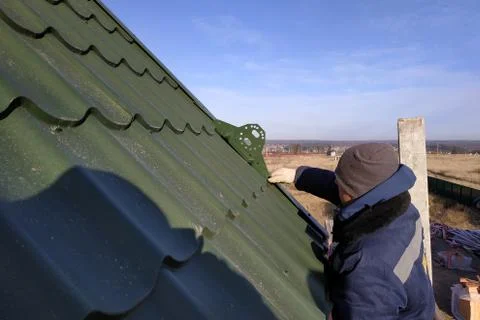The worker screws the snow retaining elements to the roof with a screwdriver Foto stock