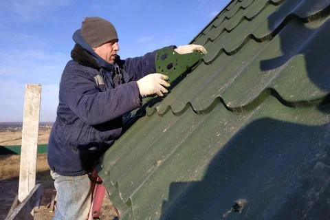 The worker screws the snow retaining elements to the roof with a screwdriver Foto stock