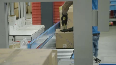 Worker Sealing Cardboard Box on Conveyor Belt for Shipping Stock Footage 329464630