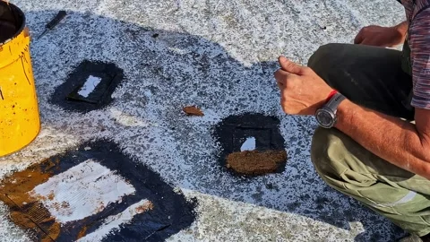 Worker sealing flat rooftop surface by hand using waterproofing material Stockbeeldmateriaal 325832347