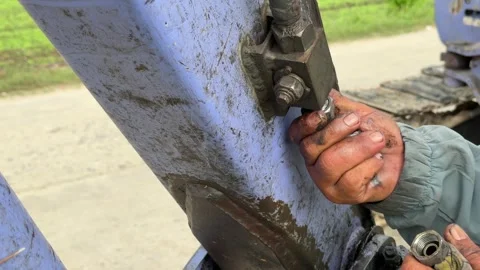 A worker secures a bolted hydraulic mounting element of an excavator using a Stock Footage 334939740