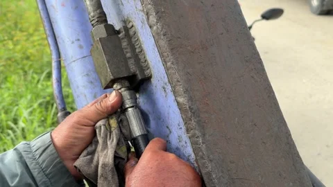 A worker secures a nut on a metal hydraulic component of an excavator with a wre Stock Footage 338001169
