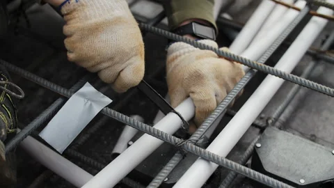 Worker securing electrical conduit with cable tie in rebar grid Stock Footage 306460420