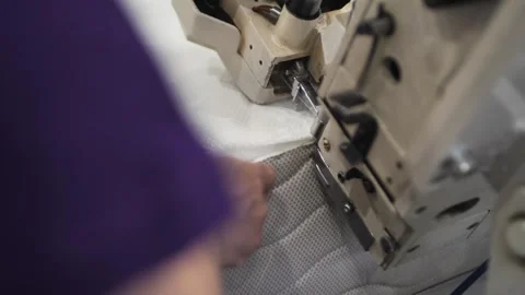 Worker sewing edges of mattress with help equipment in factory indoors. Stock Footage 240757472