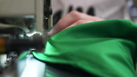 Worker sews green fabric to make hockey uniform in workshop Stock Footage 143523242