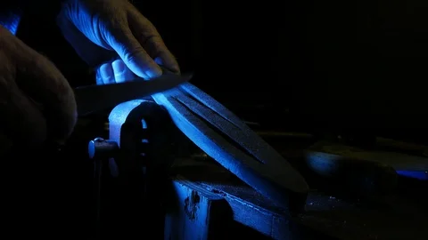 Worker sharpens a knife using whetstone in the workshop.Blue light 動画素材 103962311